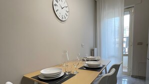 Ein Essbereich mit einem Tisch für vier Personen, Stühlen, einer Wanduhr und einer zur Außenwelt führenden Tür.