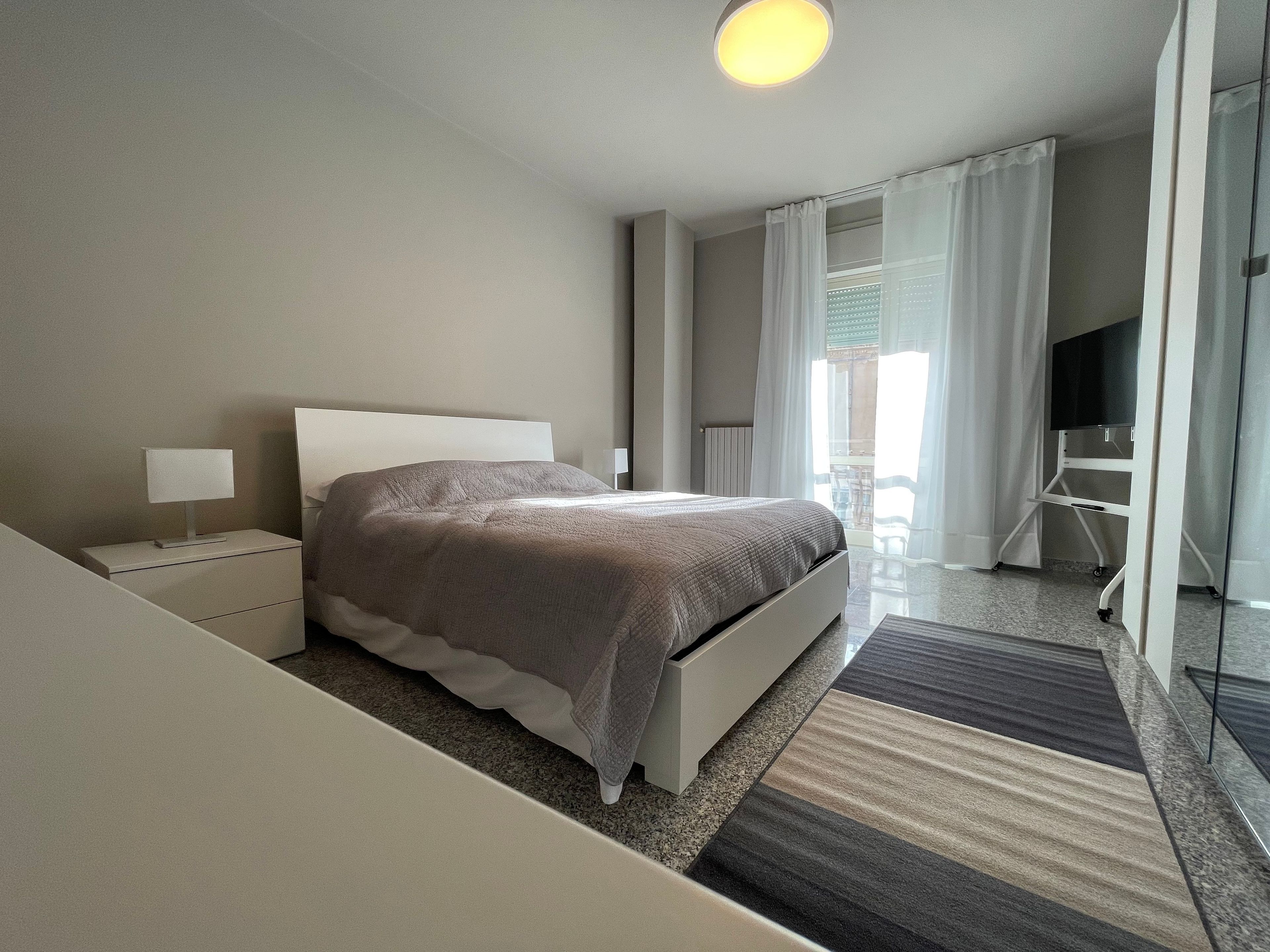 A modern hotel room with a bed, bedside tables, a flat-screen TV, and a view of the outdoors.