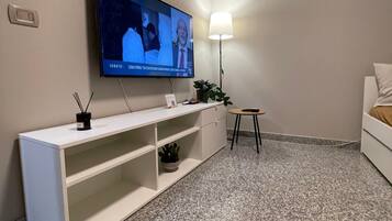 A modern living room with a flat-screen TV mounted on the wall, a white console table with a plant, a small round table with a lamp, and a white sofa.