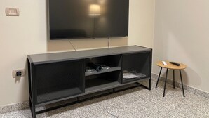 Ein modernes Wohnzimmer mit einem an der Wand befestigten Flachbildfernseher, einer schwarzen Unterhaltungsecke mit Regalen und einem kleinen runden Tisch mit Hocker.