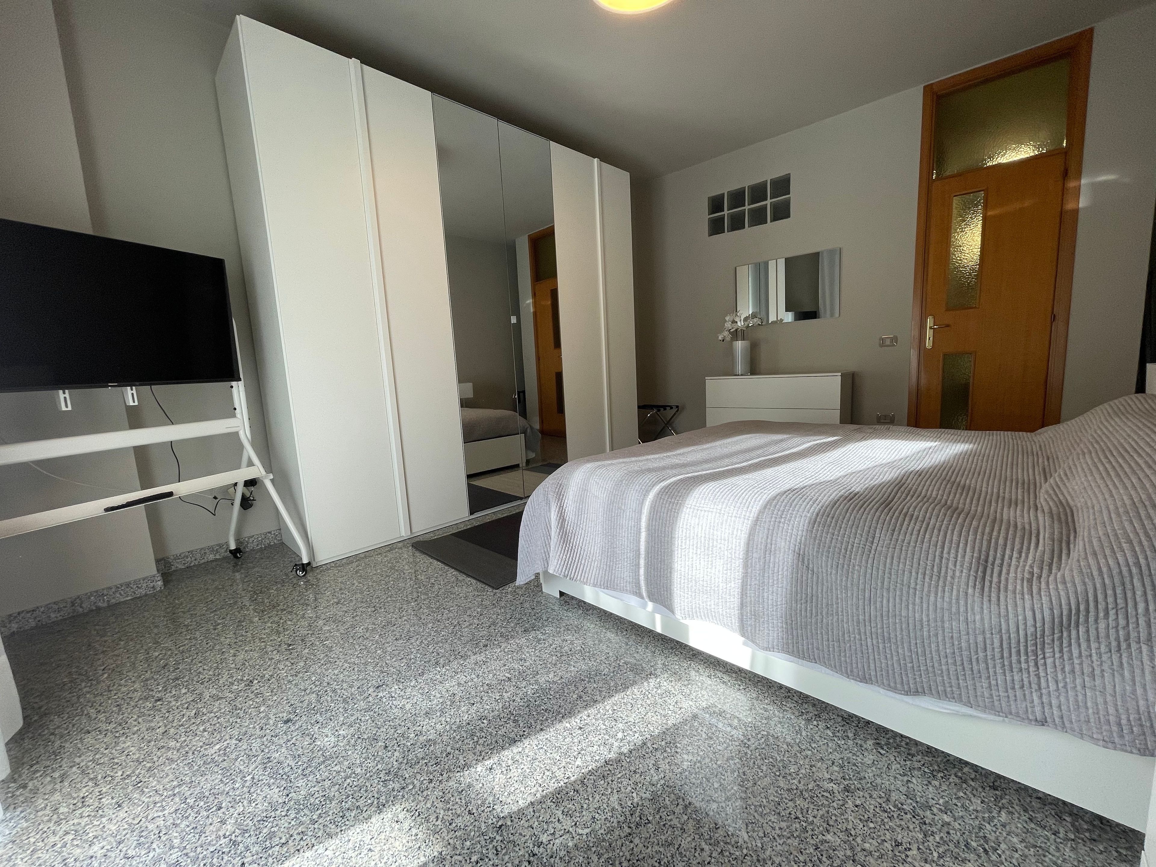Une chambre à coucher comprenant un lit, une armoire, un bureau avec un téléviseur à écran plat, un miroir et une porte.