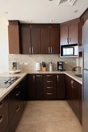 Una cocina moderna con armarios de madera oscura, un refrigerador de acero inoxidable, un microondas integrado y una encimera de granito.
