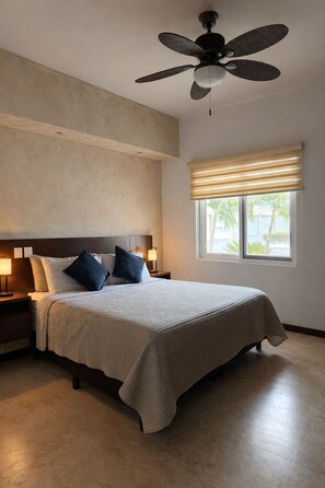 A bedroom with a bed, a ceiling fan, a nightstand with a lamp, and a window with blinds. - Oceanfront Suite (El Centenario)