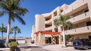 Un hotel de varios pisos con un diseño arquitectónico moderno, que cuenta con un área de entrada cubierta y palmeras.
