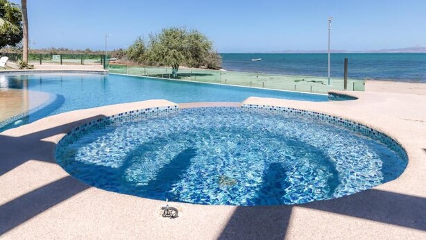 Una piscina con vista al mar, rodeada de arena y vegetación.