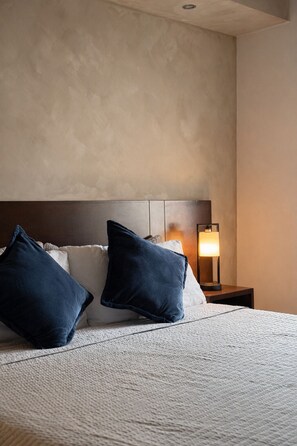 Una habitación de hotel con cama, almohadas, mesita de noche y lámpara.