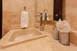 A bathroom with a large bathtub, a sink with a chrome faucet, and a mirror. There is a towel hanging on a ring, and a soap dish with a bar of soap. - Oceanfront Suite (El Centenario)
