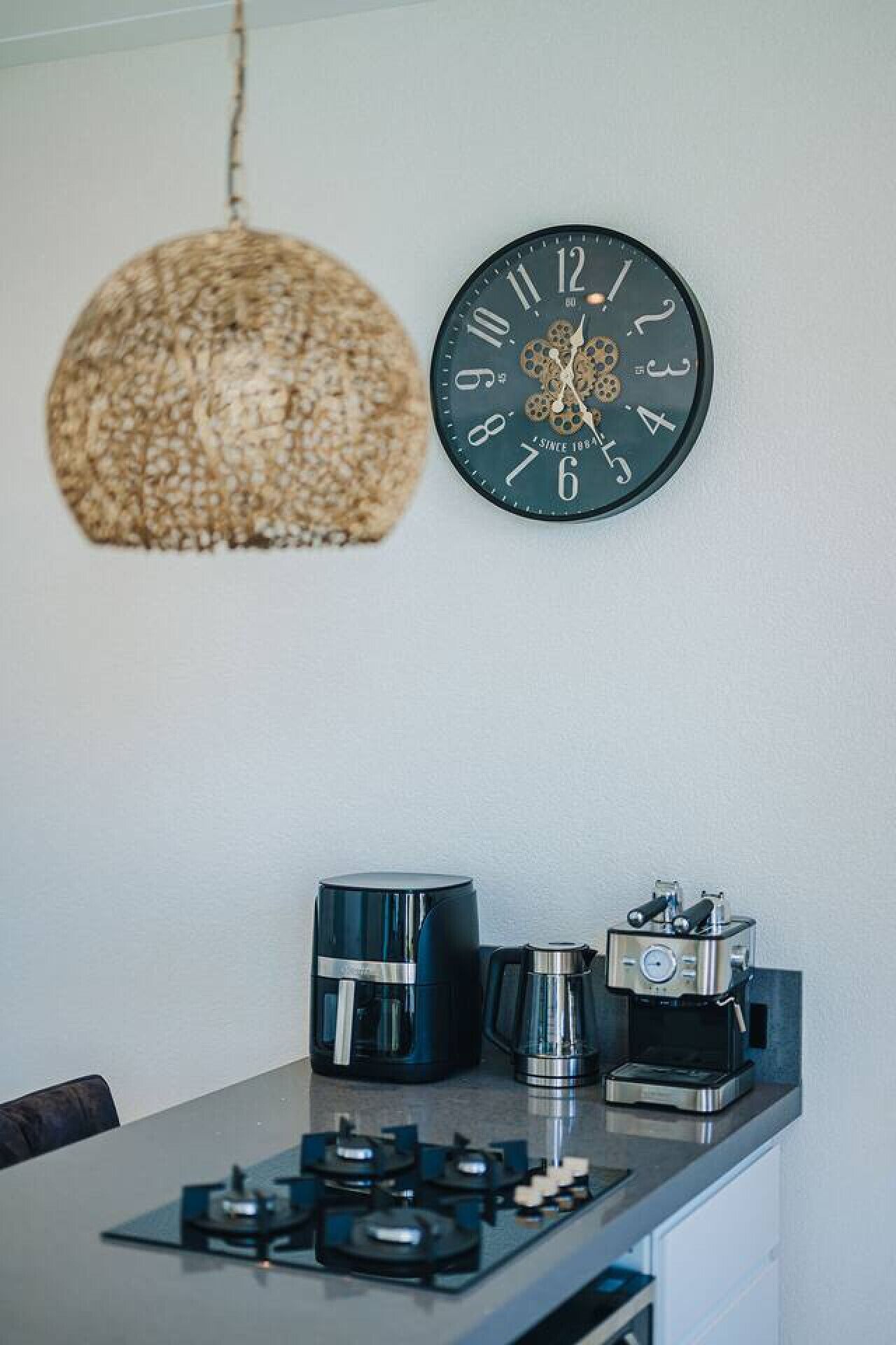 A kitchen with a hanging light fixture, a wall clock, and coffee-making equipment.
