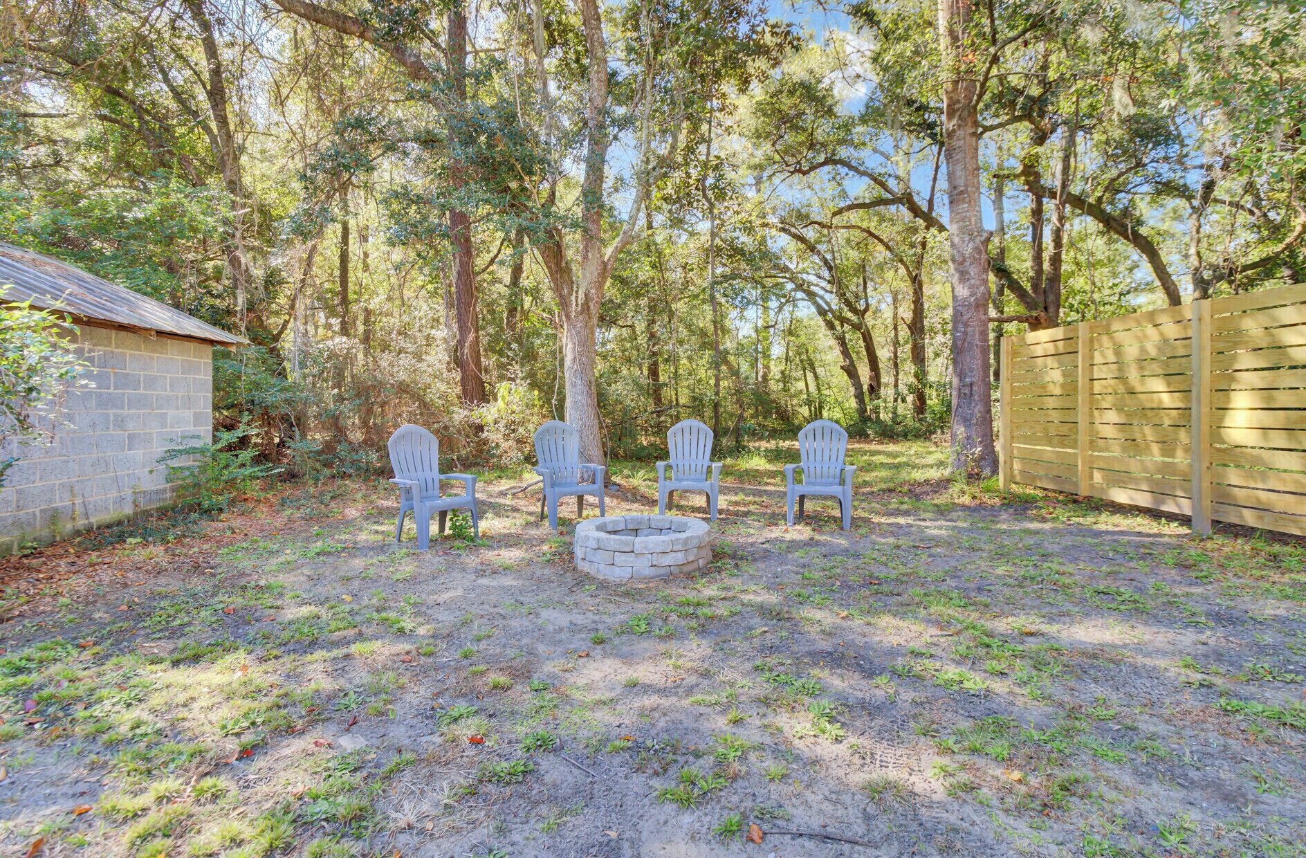 A backyard with four Adirondack chairs, a stone fire pit, and a wooden fence.