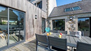 Un espace de restauration extérieur moderne, doté d’une terrasse en bois, d’une table avec des chaises et d’un mur en pierre.