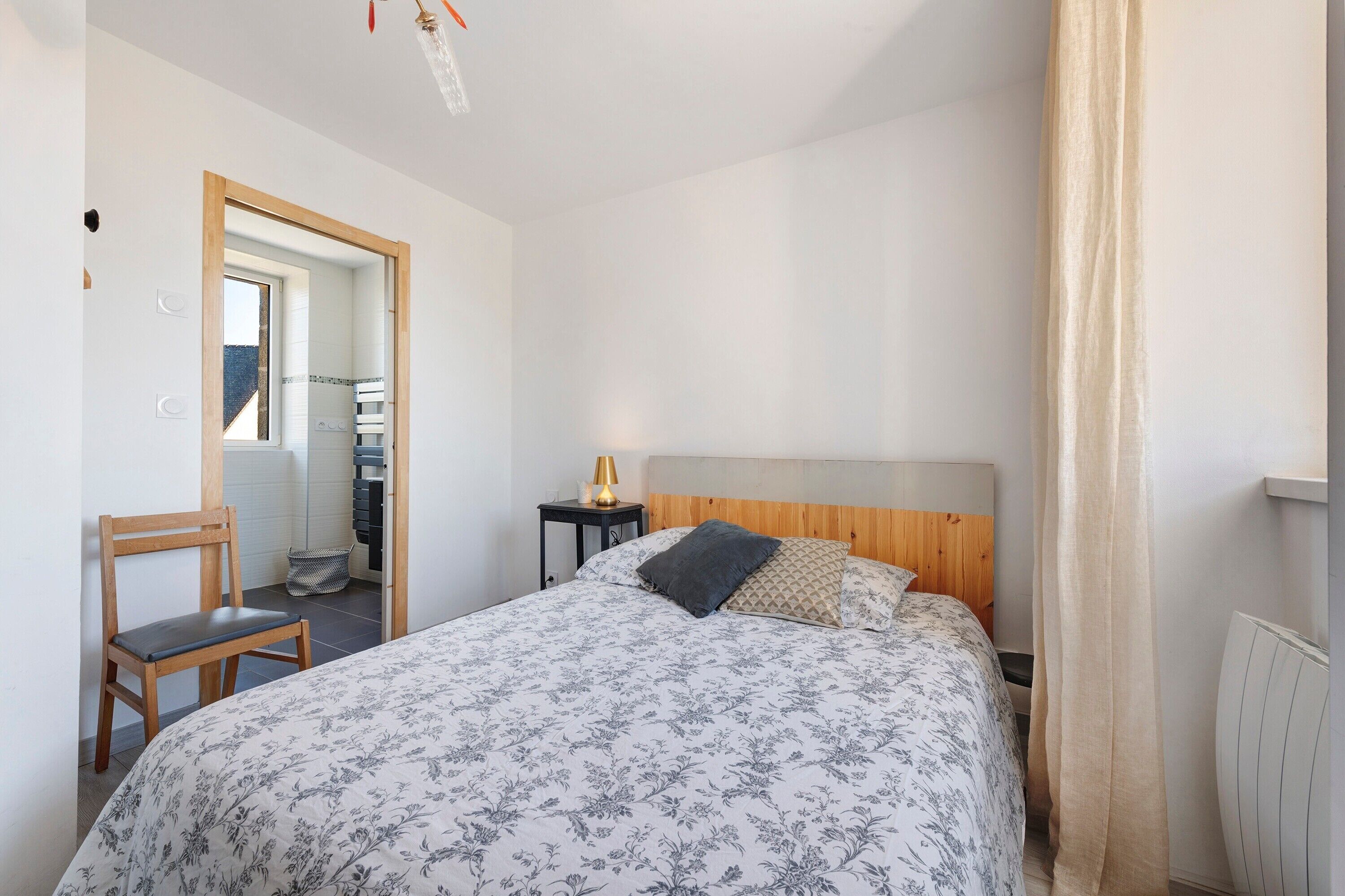 A bedroom with a bed, a chair, a bedside table with a lamp, and a radiator.