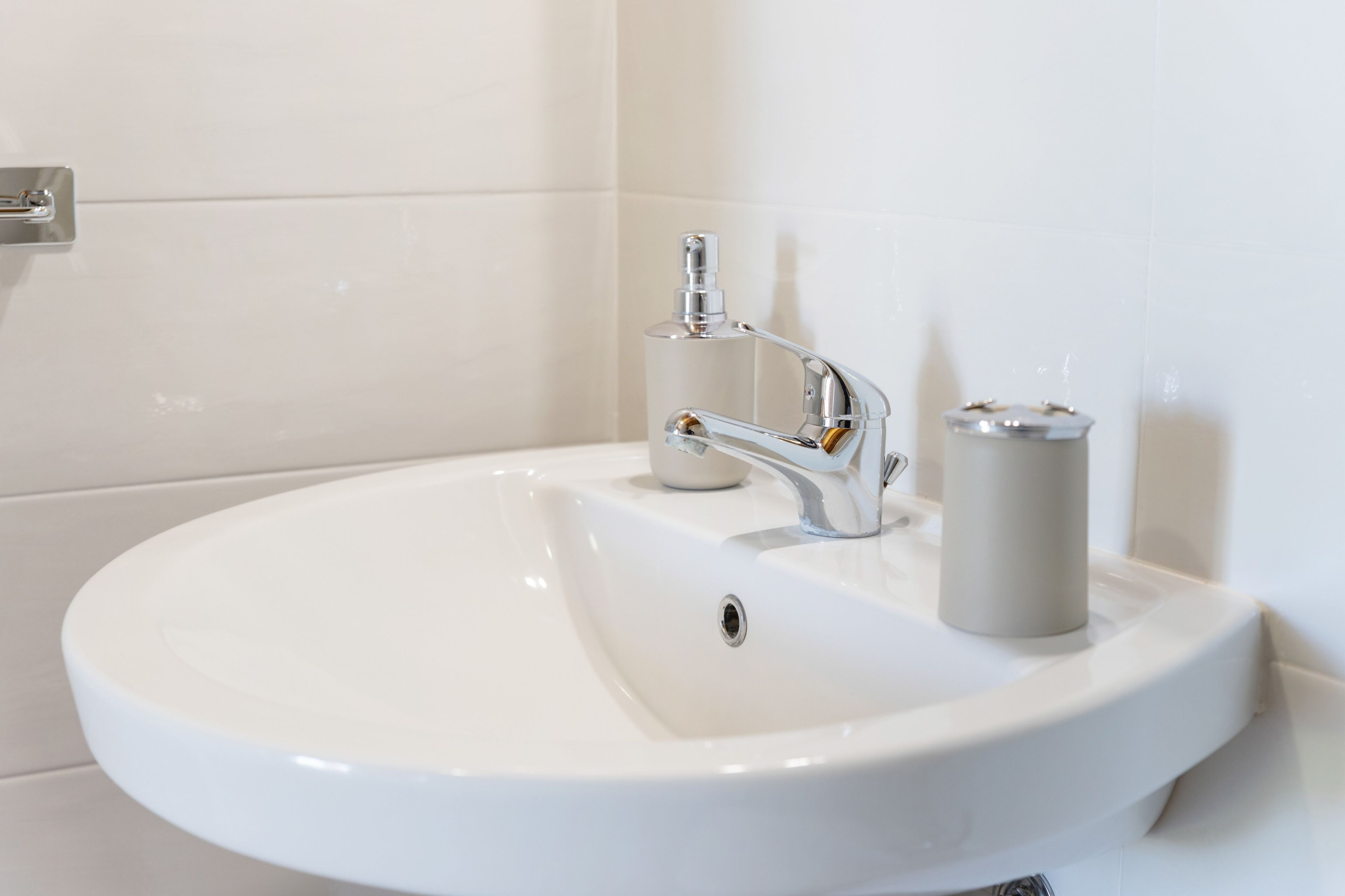Un lavabo blanc pour la salle de bain, doté d’un robinet chromé et d’un distributeur de savon cylindrique.