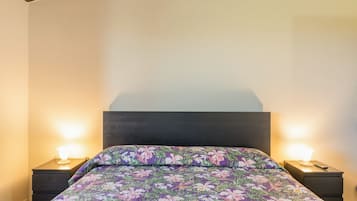 Ein Bett mit floralem Überwurf, zwei Nachttischlampen und ein dunkles Kopfteil.