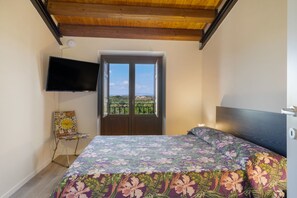 A bedroom with a bed, a chair, a TV, and a door leading to a balcony. - Room 'Vigna Di Pettineo - N5' with Shared Pool, Private Terrace and Air Conditioning (Vittoria)