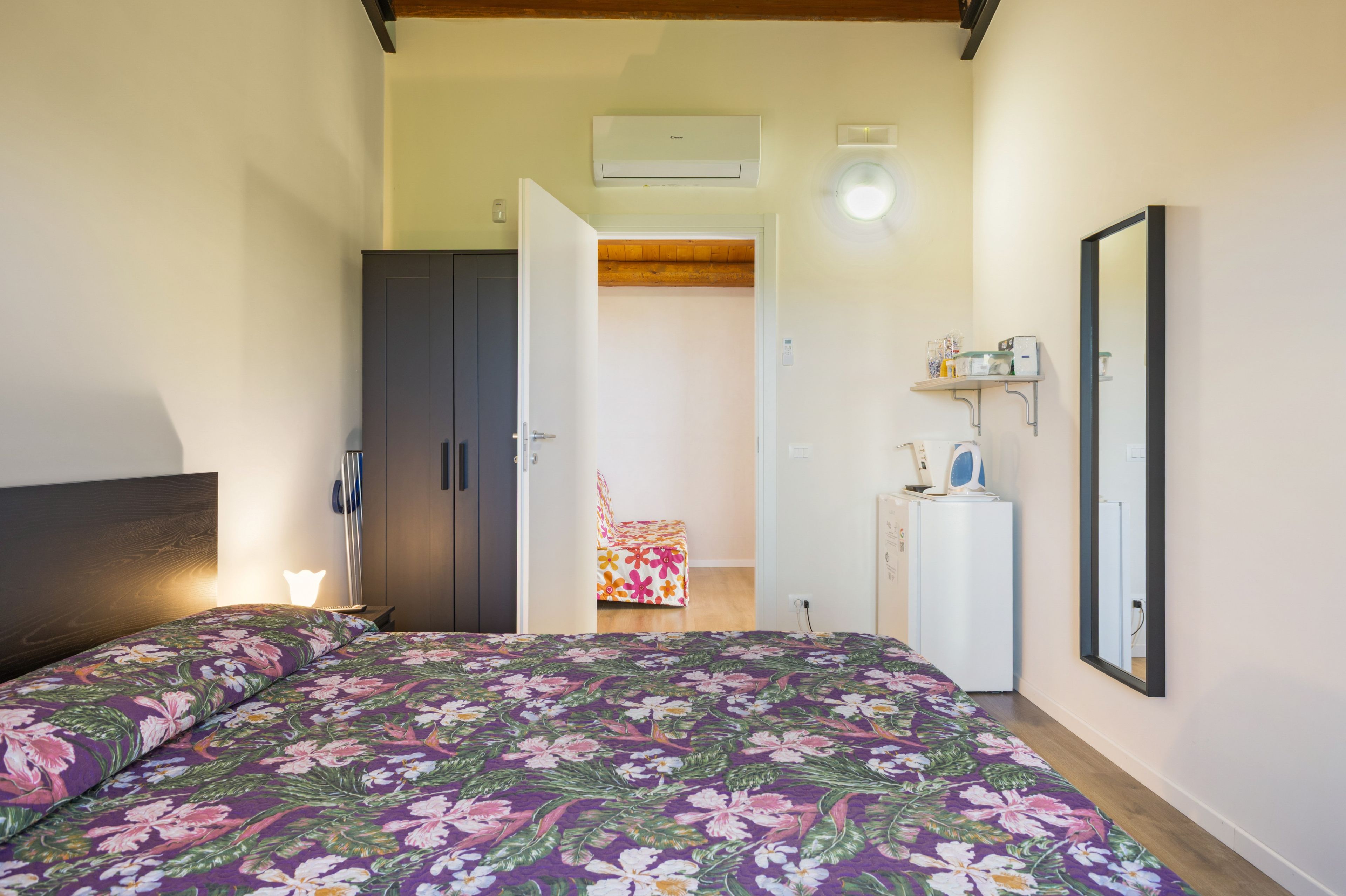 Quarto com cama, guarda-roupa e pequena área de cozinha.