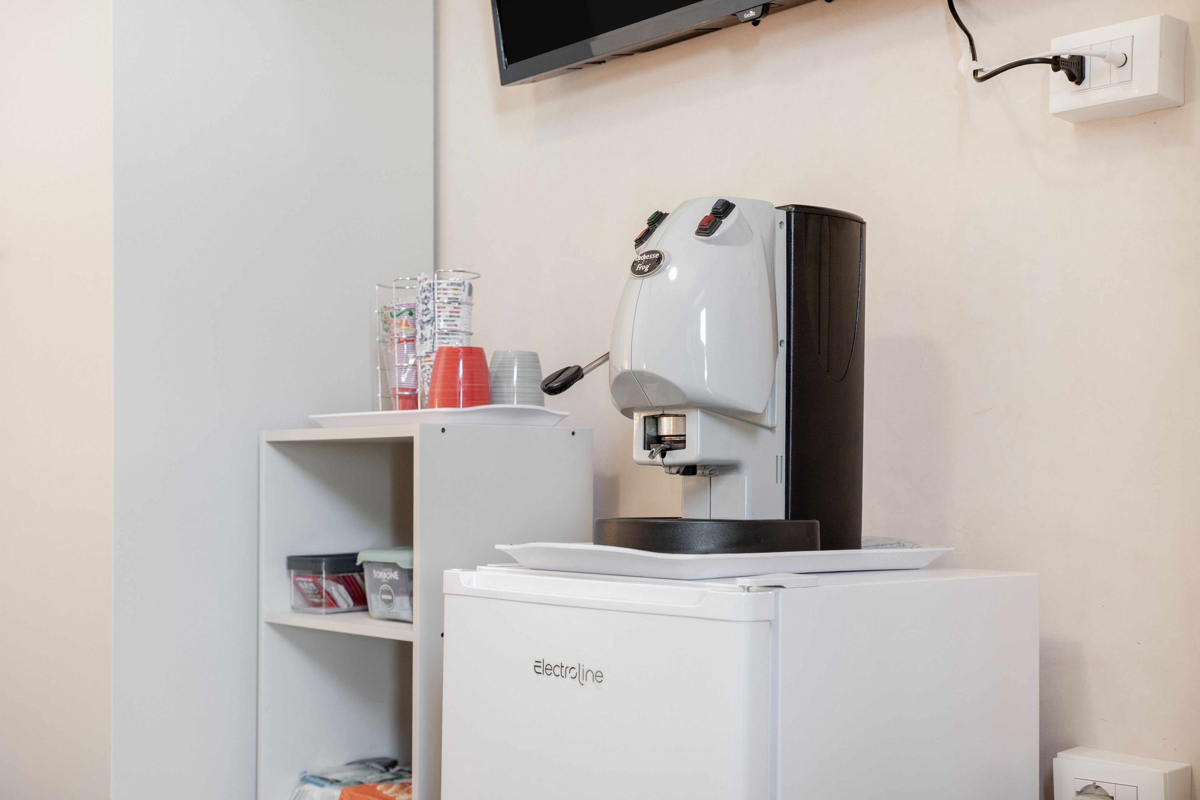 Eine kleine Küchenzeile mit einer Kaffeemaschine, einem kleinen Kühlschrank und einem Regal mit Küchenutensilien.