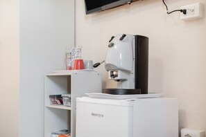 Eine kleine Küchenzeile mit einer Kaffeemaschine, einem kleinen Kühlschrank und einem Regal mit Küchenutensilien.