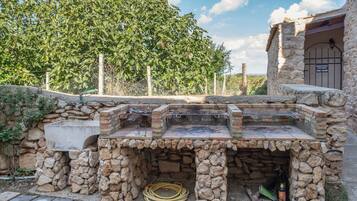 Zona de parrilla exterior con paredes de piedra y acceso a la piscina.