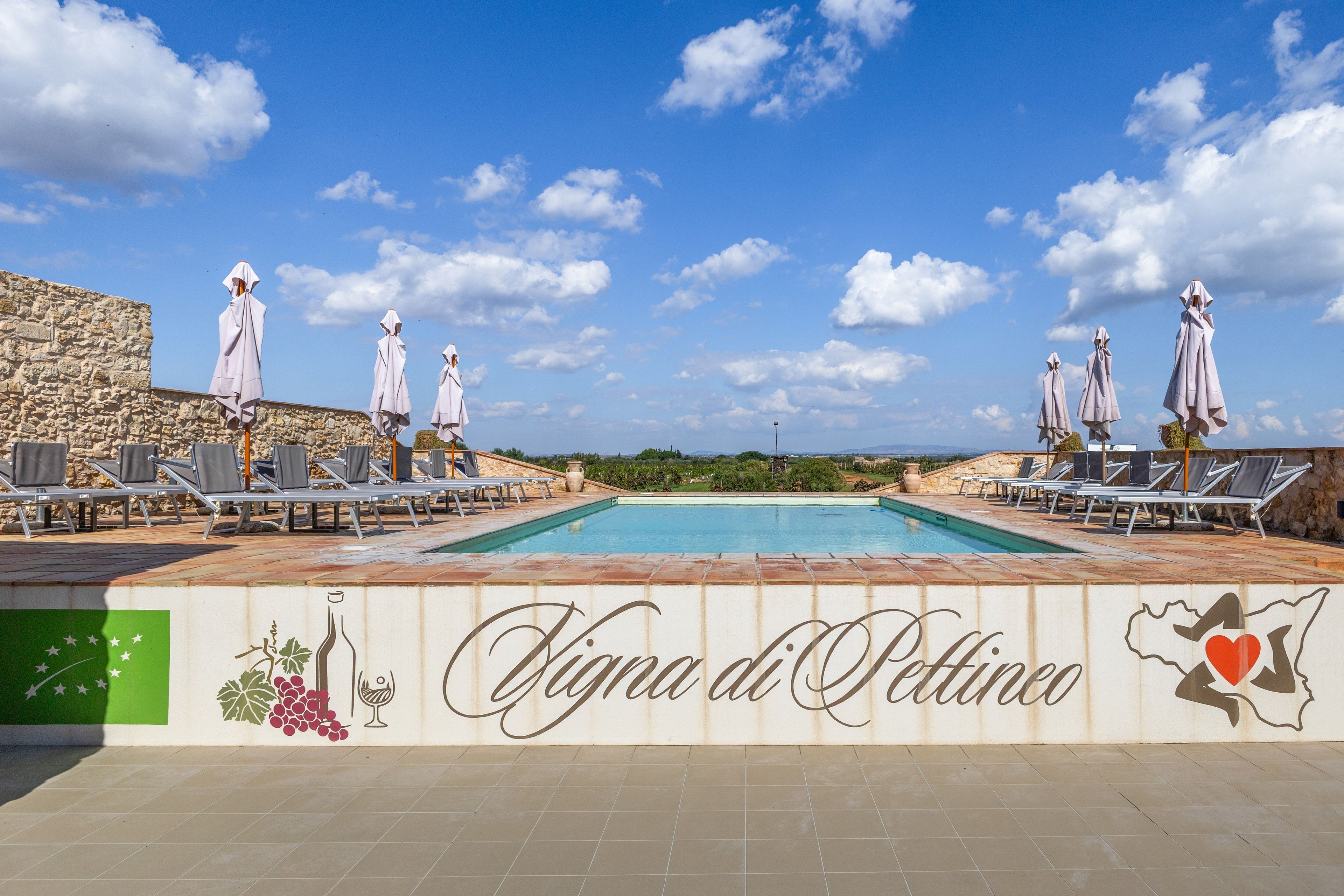Ein Poolbereich mit Liegestühlen und Sonnenschirmen, eine Steinmauer und ein Schild mit der Aufschrift 'Villa di Pettino'.