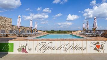 Ein Poolbereich mit Liegestühlen und Sonnenschirmen, eine Steinmauer und ein Schild mit der Aufschrift 'Villa di Pettino'.