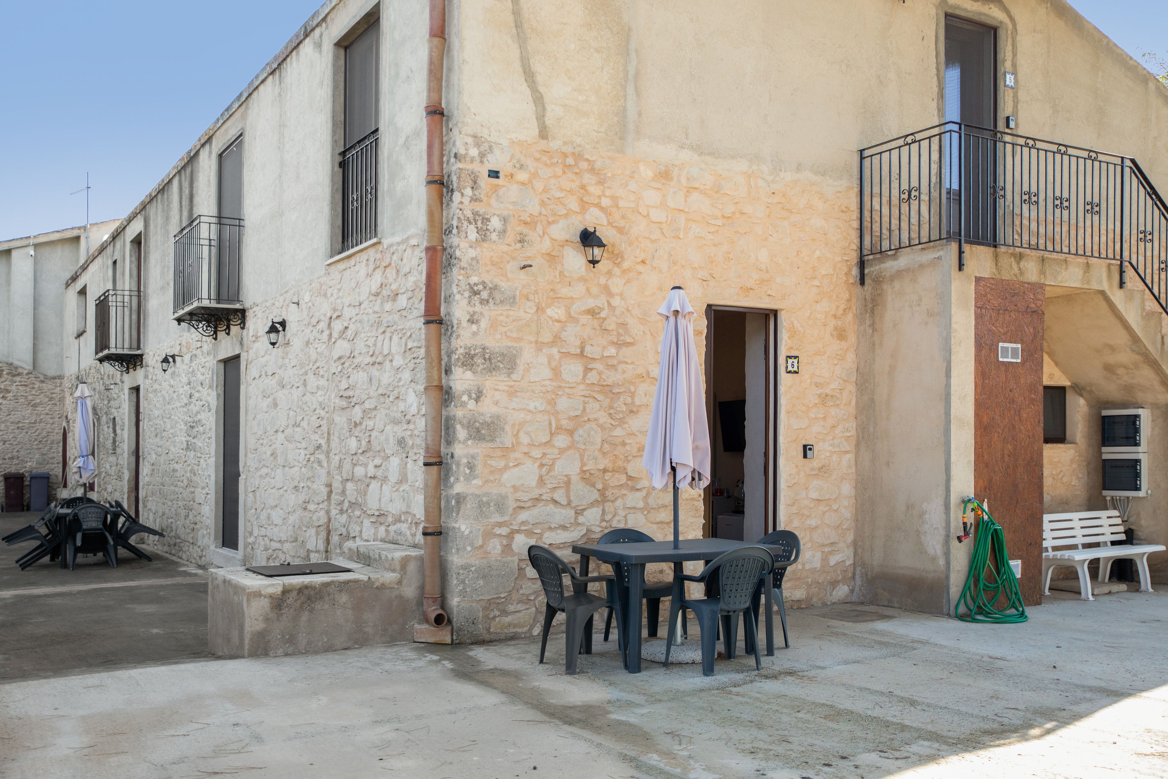 A building with a stone facade, outdoor seating area with tables and chairs, and a small balcony with a railing.