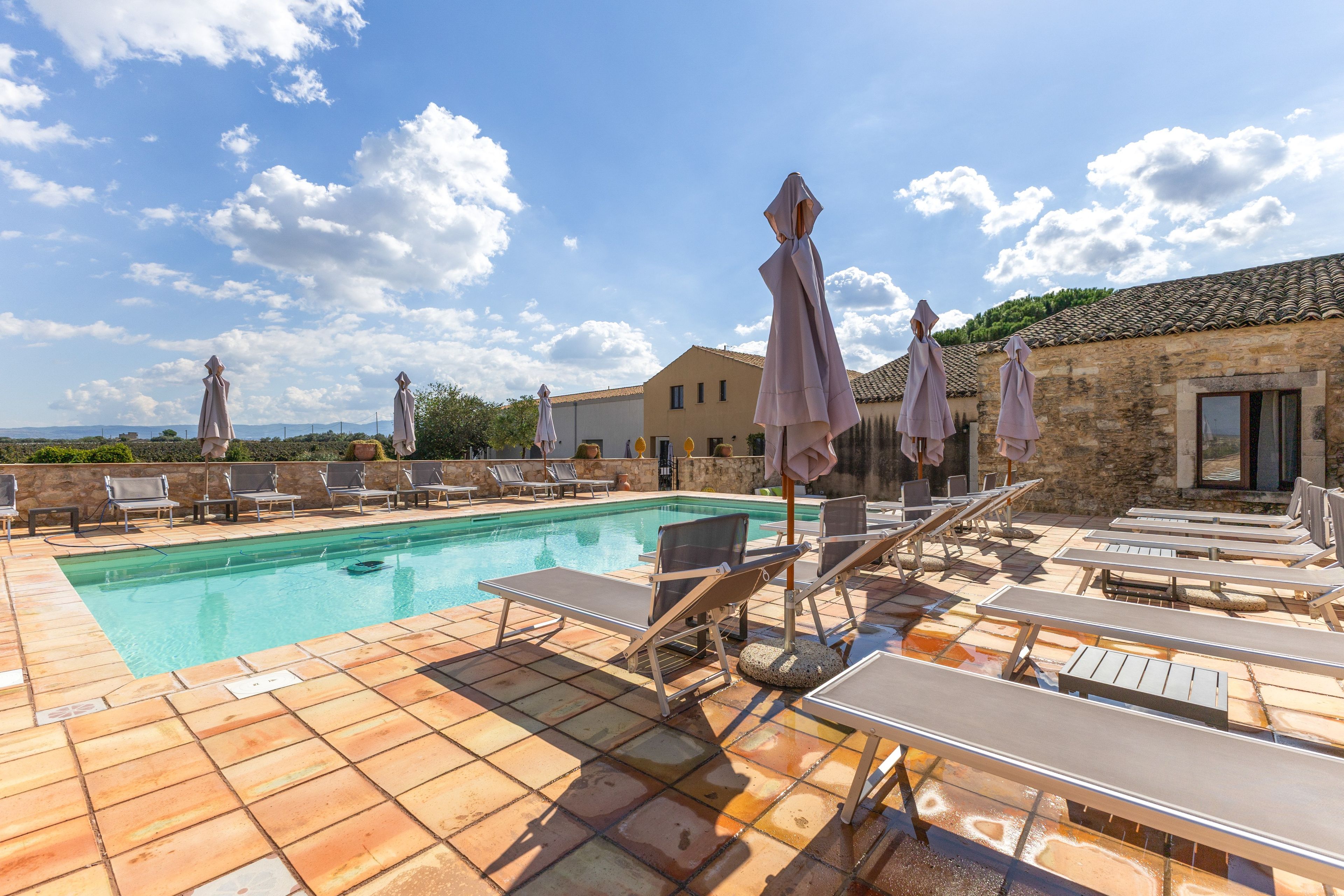 A poolside area with lounge chairs and umbrellas, a swimming pool, and a stone building in the background.