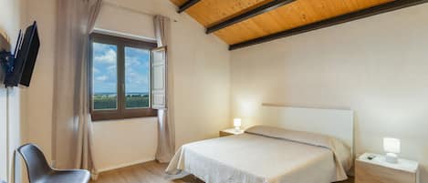 A bedroom with a bed, bedside table, lamp, chair, window with curtains, and a TV mounted on the wall.