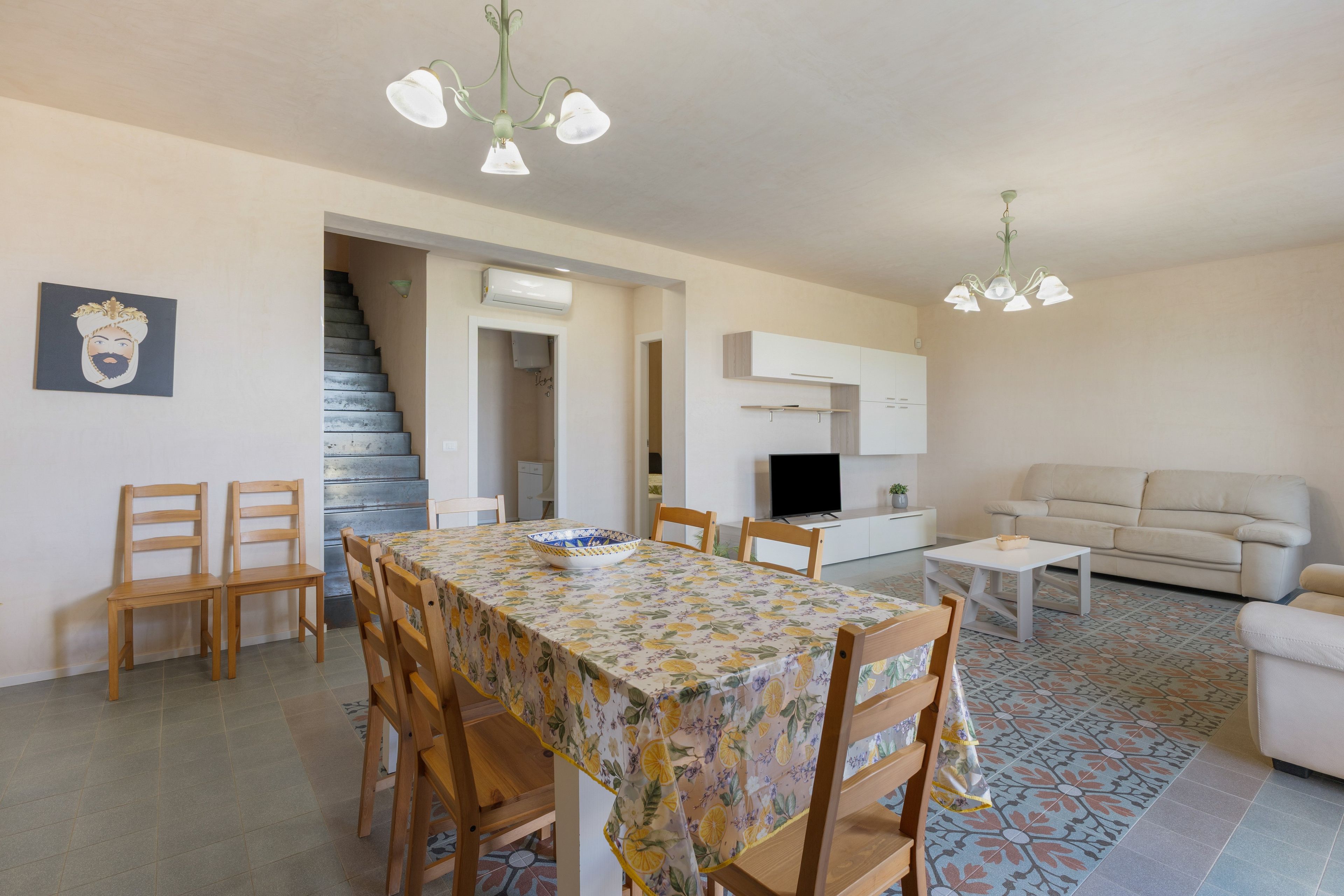 Un comedor con una mesa y sillas, una escalera, una sala de estar con un sofá y un televisor.