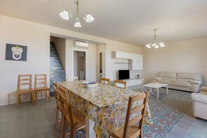 Un comedor con una mesa y sillas, una escalera, una sala de estar con un sofá y un televisor.