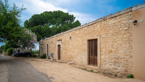 A stone building with a dirt path, a parked car, and a large tree.