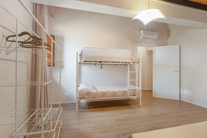 Ein Etagenbett mit weißem Kopfteil, ein Metallregal mit Kleidung und eine Tür im Hintergrund.