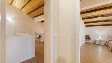 Un interior moderno con techo inclinado, piso de madera y cama con mesita de noche y lámpara.