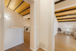 Un interior moderno con techo inclinado, piso de madera y cama con mesita de noche y lámpara.