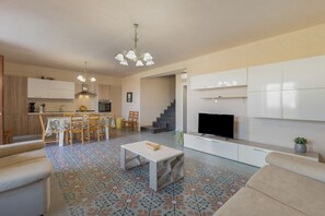 Ein modernes Wohnzimmer mit Flachbildfernseher, eine Essecke mit Tisch und Stühlen sowie eine Küche mit Schränken und Herd.