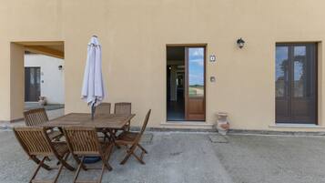 Eine Terrasse im Freien mit Holztisch und -stühlen, einem weißen Sonnenschirm und Blick auf die Landschaft durch die offene Tür.