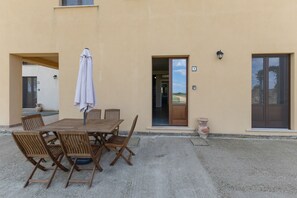 Eine Terrasse im Freien mit Holztisch und -stühlen, einem weißen Sonnenschirm und Blick auf die Landschaft durch die offene Tür.