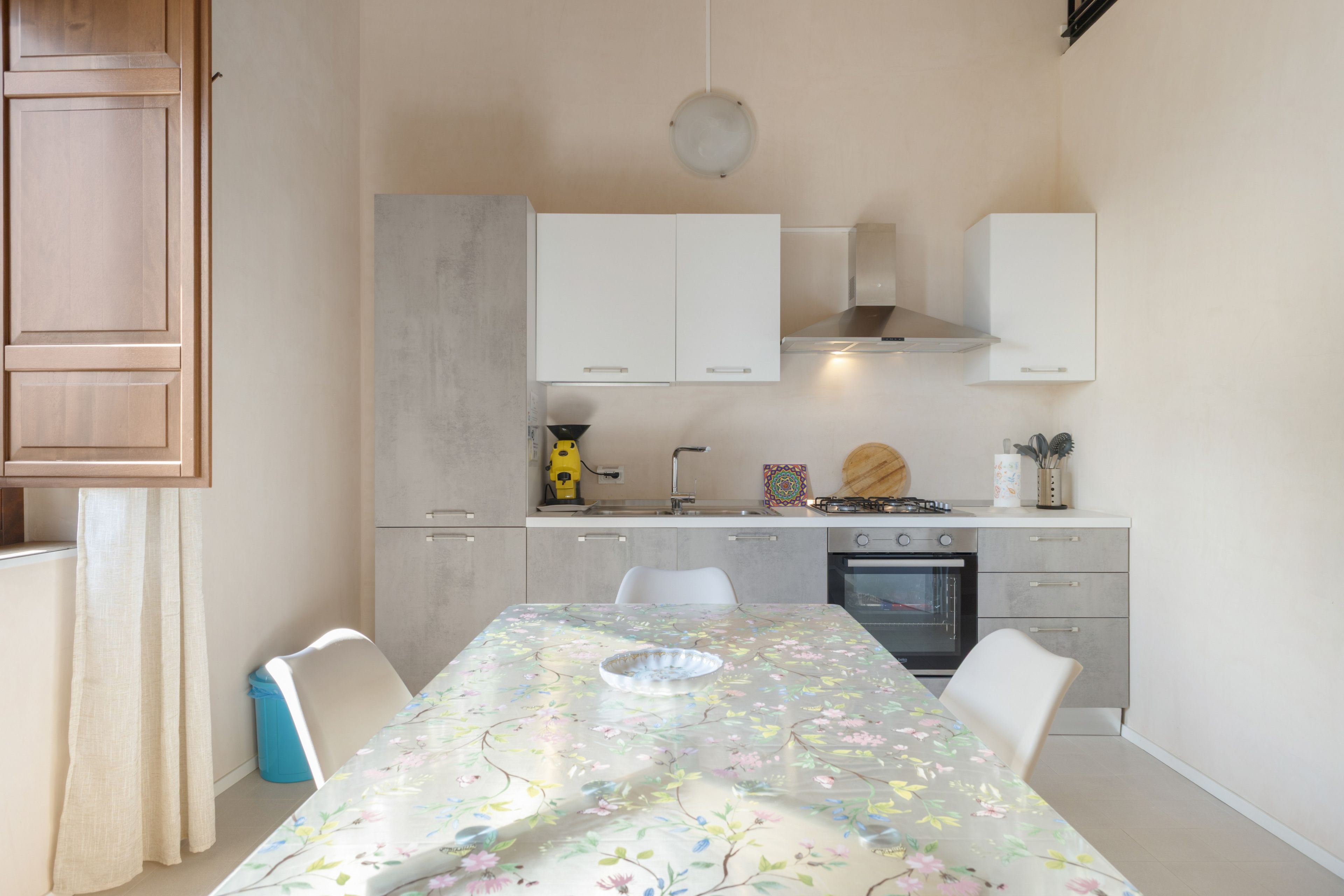 Une cuisine moderne avec des meubles blancs, une cuisinière à gaz et une table à manger recouverte d’une nappe à motifs floraux.
