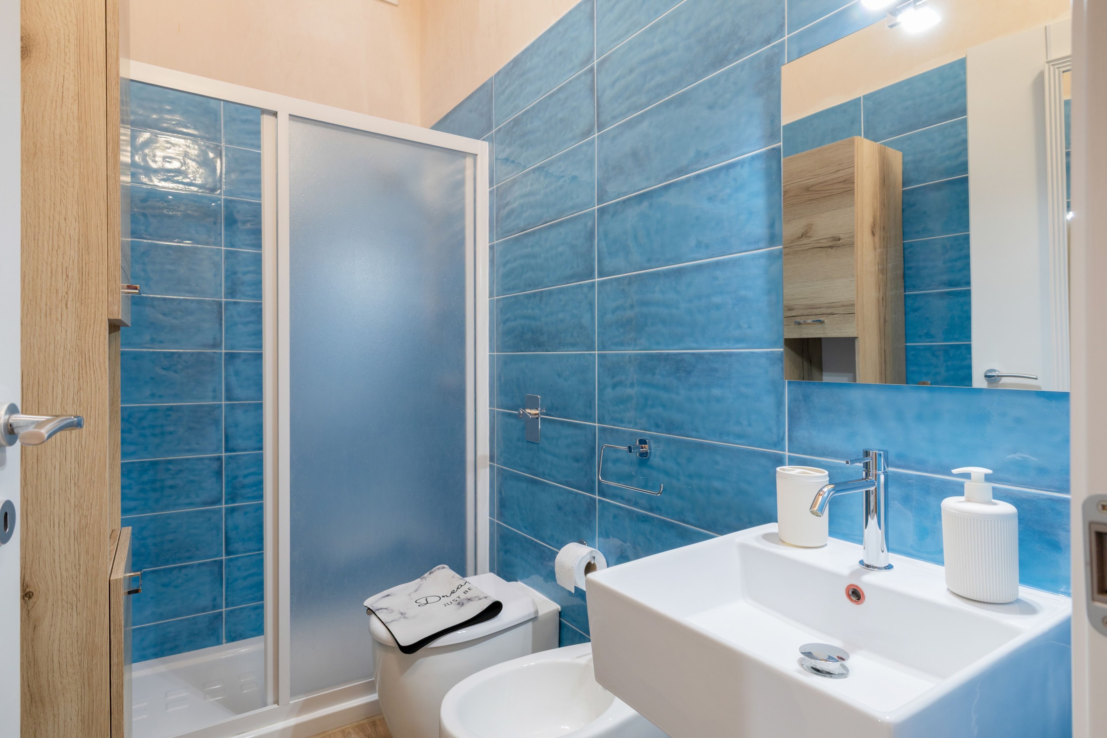 Un baño con azulejos azules, un lavabo blanco, un espejo y una ducha.