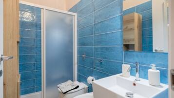 Un baño con azulejos azules, un lavabo blanco, un espejo y una ducha.