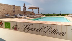 Zwembad met ligbedden en parasols, een stenen muur en een bordje met de tekst 'Vigna di Pettino'.
