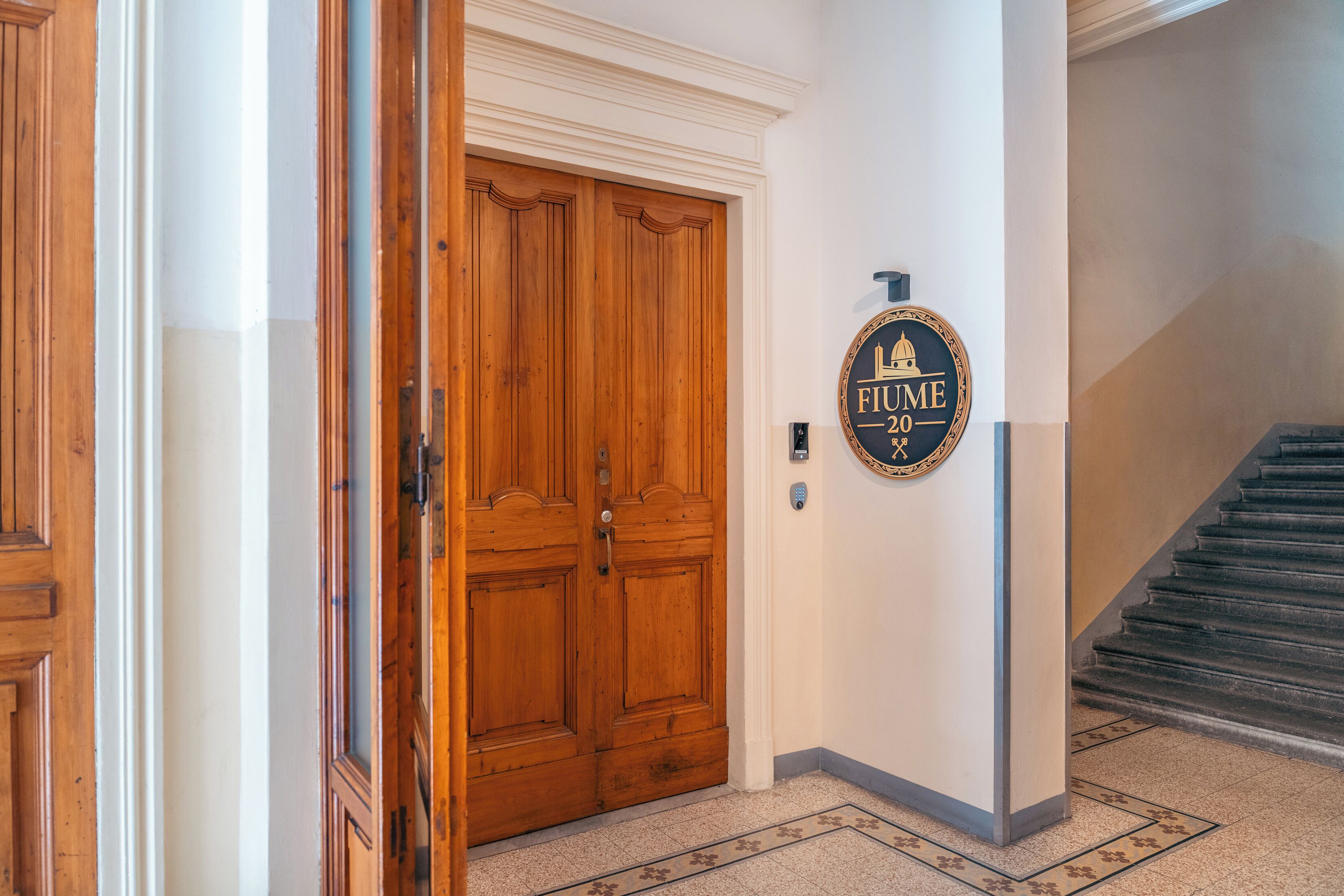 Una puerta de madera con una placa que dice 'FIUME 20' y una escalera que lleva a un piso superior.