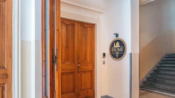 Una puerta de madera con una placa que dice 'FIUME 20' y una escalera que lleva a un piso superior.