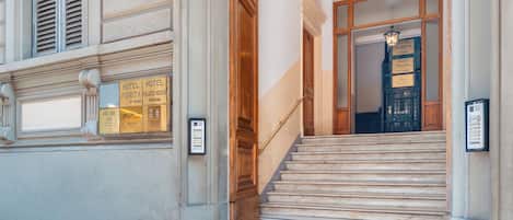 A hotel entrance with a marble staircase, a wooden door, and a sign indicating the hotel name and room types.