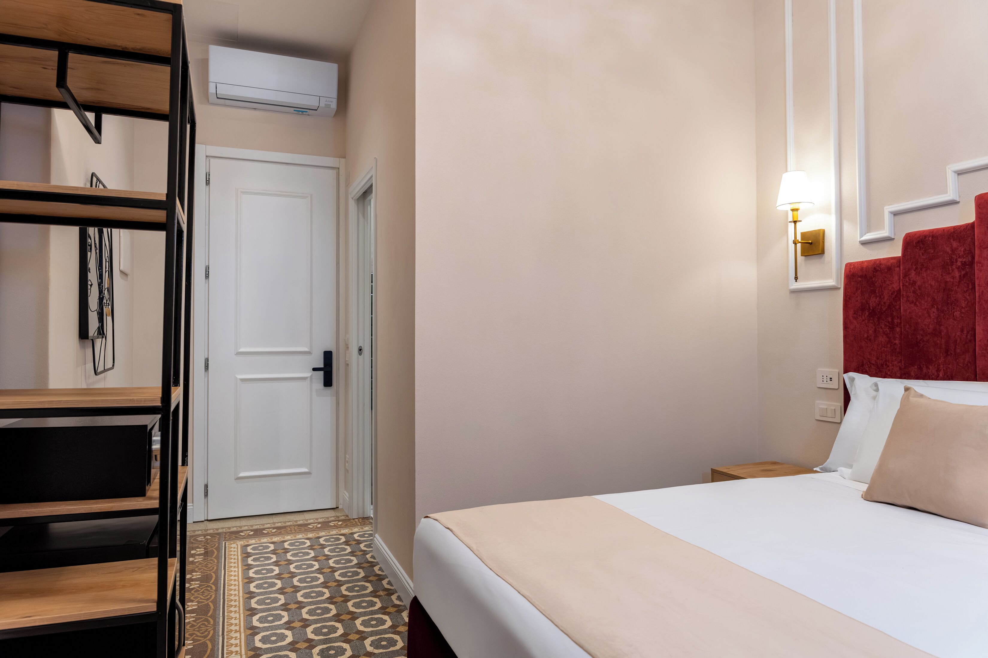 A hotel room with a bed, a wardrobe, a door, and a patterned floor.