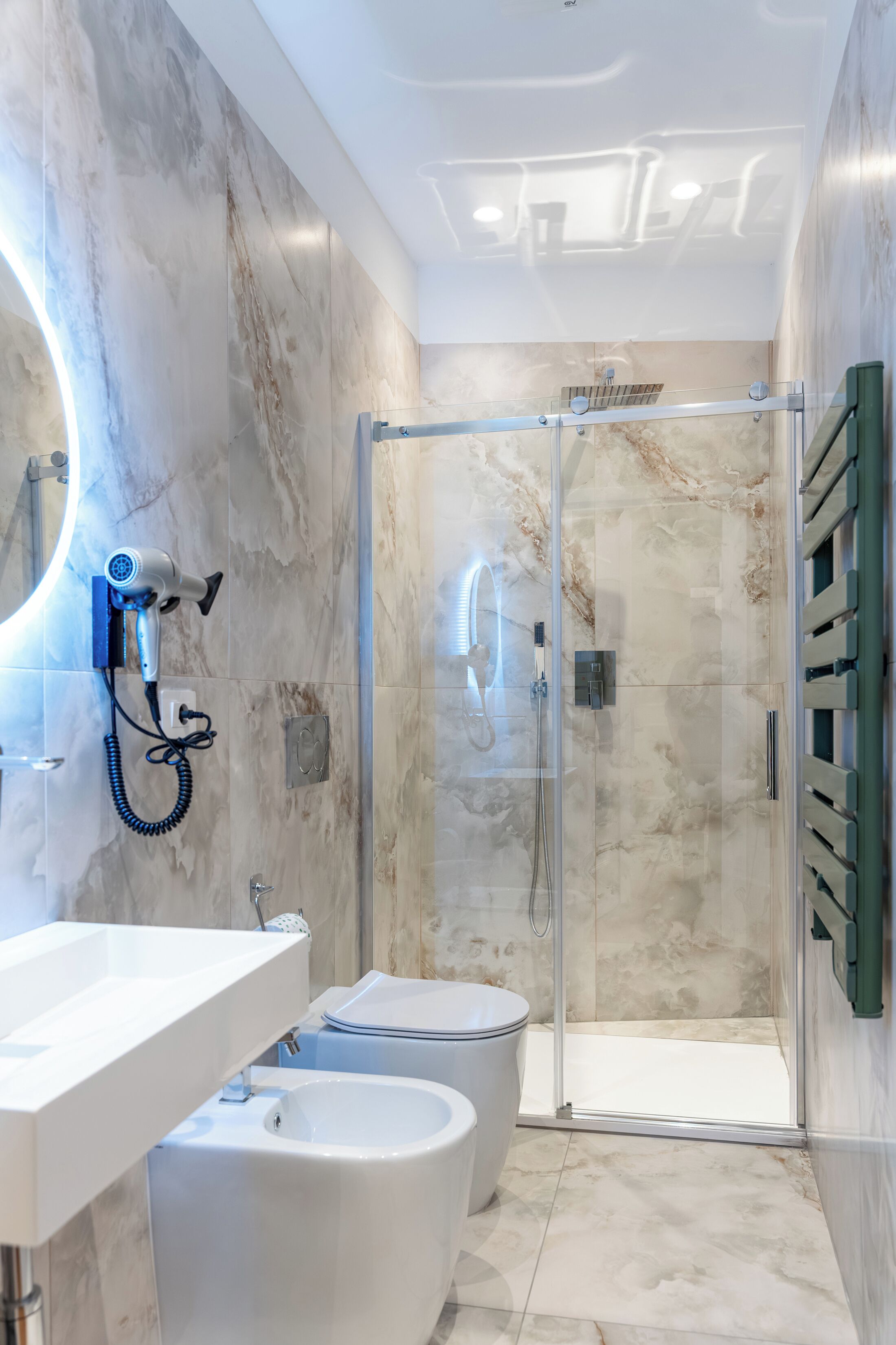 A modern bathroom with a marble wall, a glass-enclosed shower, a white sink, and a bidet.