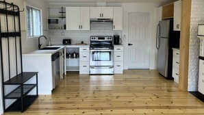 Eine kompakte Küche mit weißen Schränken, einem Edelstahlbackofen, einem Kühlschrank und Holzboden.