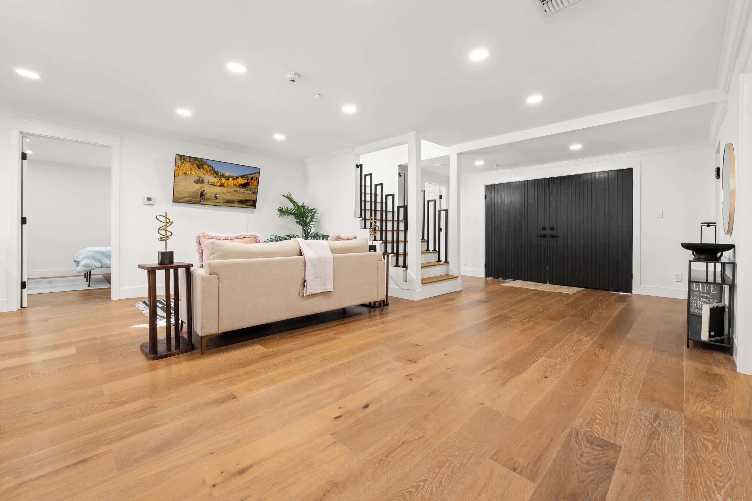 A spacious living area with a wooden floor, a beige sofa, a painting, and a staircase.