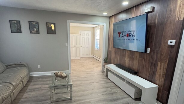 Uma sala de estar moderna com uma grande televisão de tela plana fixada em uma parede de madeira, um sofá modular cinza e uma mesa de centro de vidro.