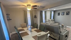 Uma sala de jantar com uma mesa, cadeiras, um ventilador de teto e um sofá.