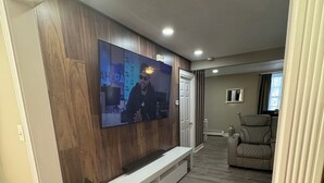 Uma sala de estar moderna com uma TV de tela plana fixada numa parede de madeira, um banco branco e um sofá de couro.